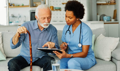 Doctor or nurse caregiver with senior man holding walking cane at home or nursing home